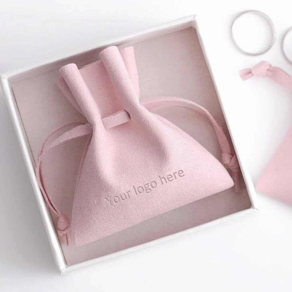 Pink microfiber jewelry pouch with debossed logo for luxury brand identity, high-quality drawstring packaging.