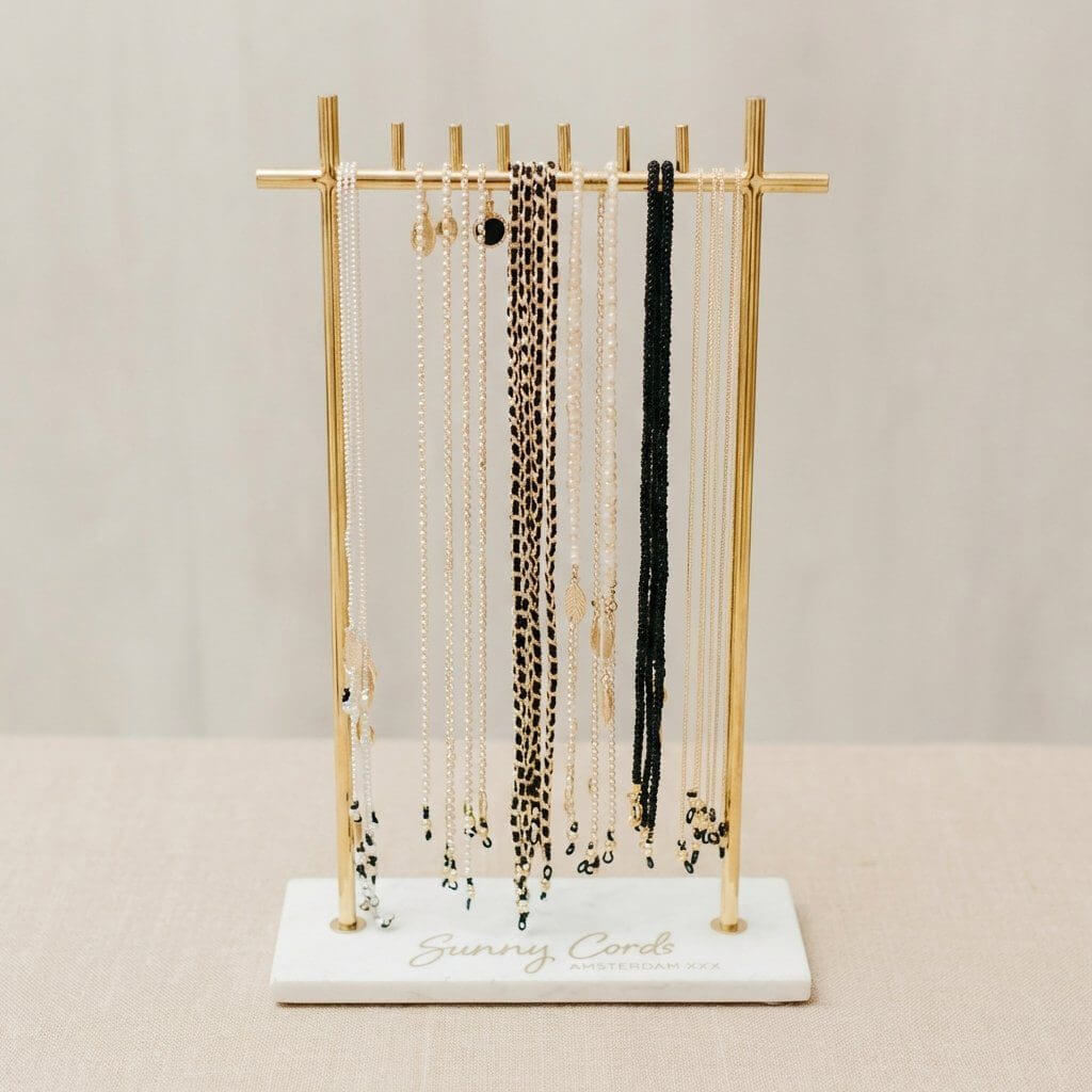 Gold T-bar jewelry display stand with white marble base for long necklaces and retail accessories.
